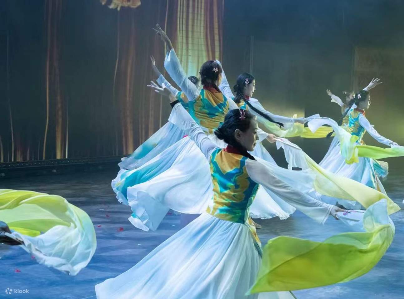 Les actrices dansent en longues robes dégradées, leurs longues manches flottent, une lumière chaude soulignant le rythme de la scène, à la fois doux et dynamique.